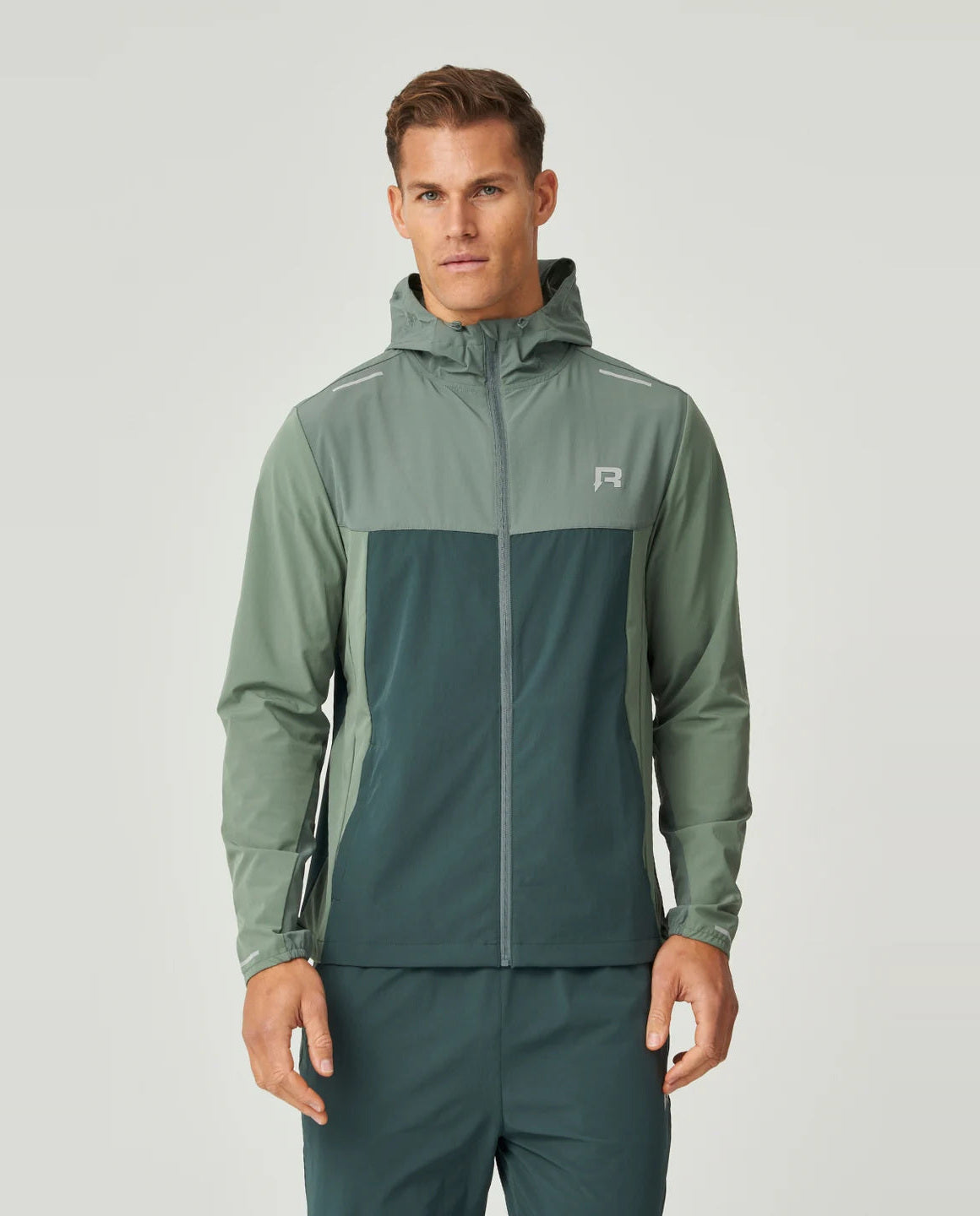 Man wearing a green windbreaker jacket with a reprimo brand logo on chest on a light grey background