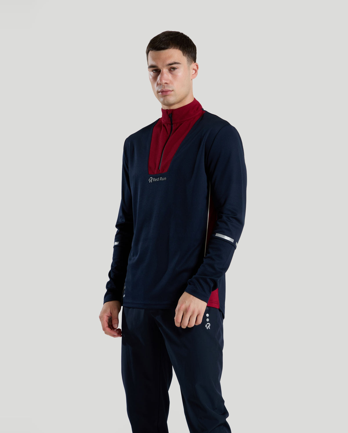 Man wearing a navy t1/4 zip tracksuit top with red accents on a light gray background