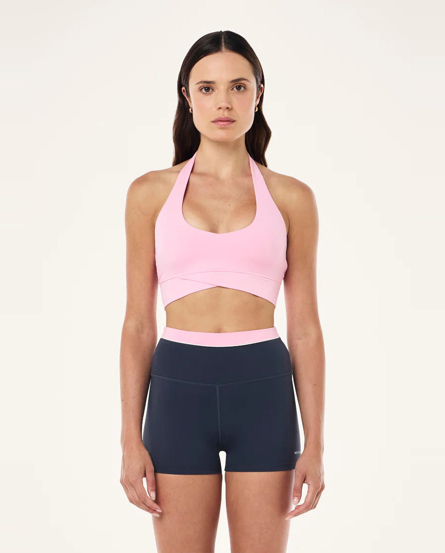 Woman wearing a pink sports bra and navy shorts on a beige background