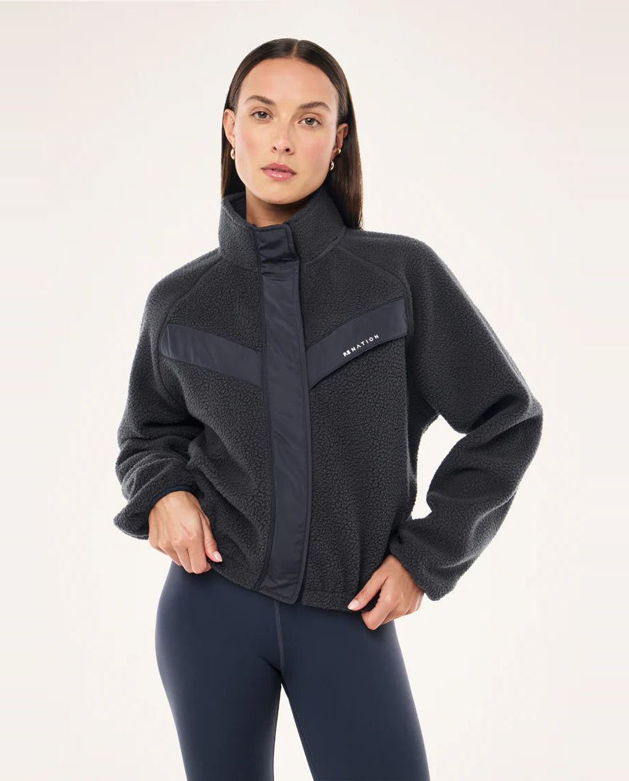Woman wearing a dark gray jacket with a brand logo on a white background