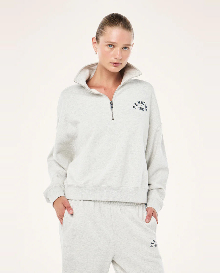 Woman wearing a light gray P.E nation tracksuit with a brand logo on a white background