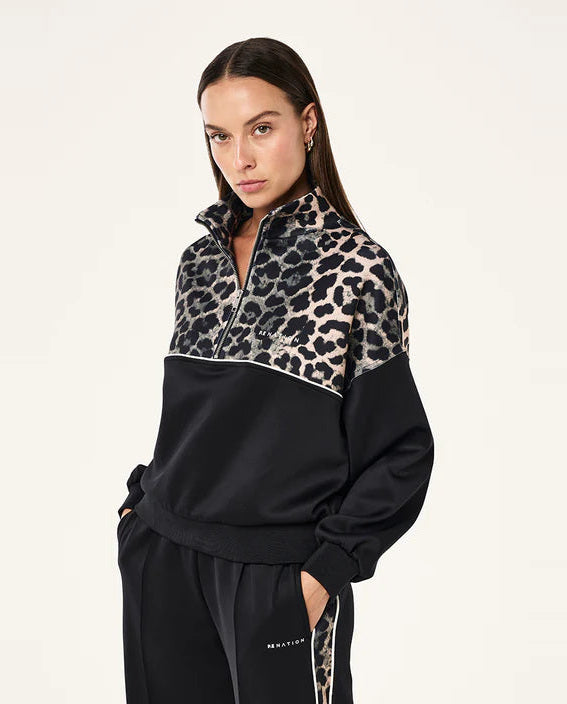 Woman wearing a black and leopard print half-zip sweatshirt on a white background
