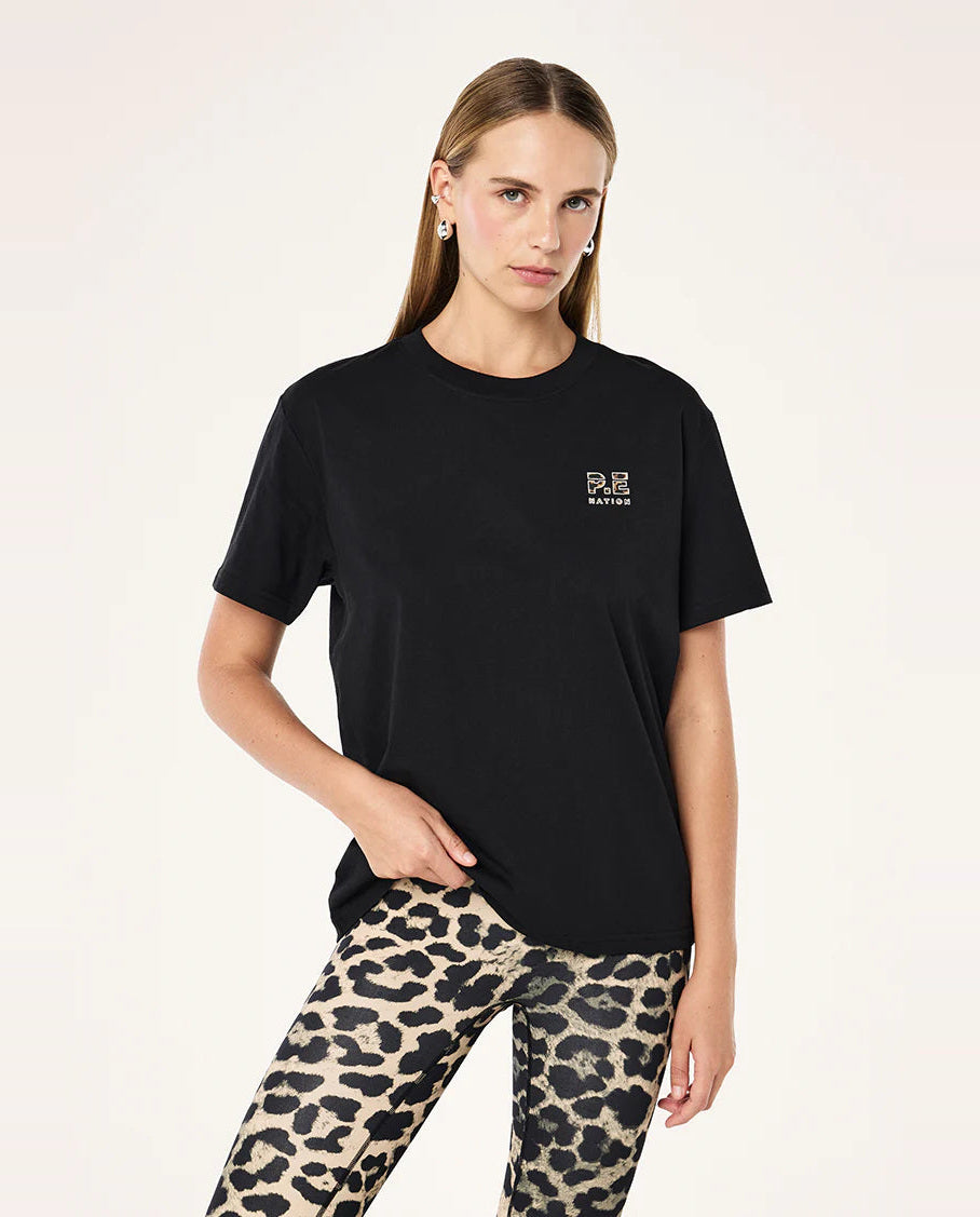 Woman wearing a black t-shirt with a logo and leopard print pants on a white background