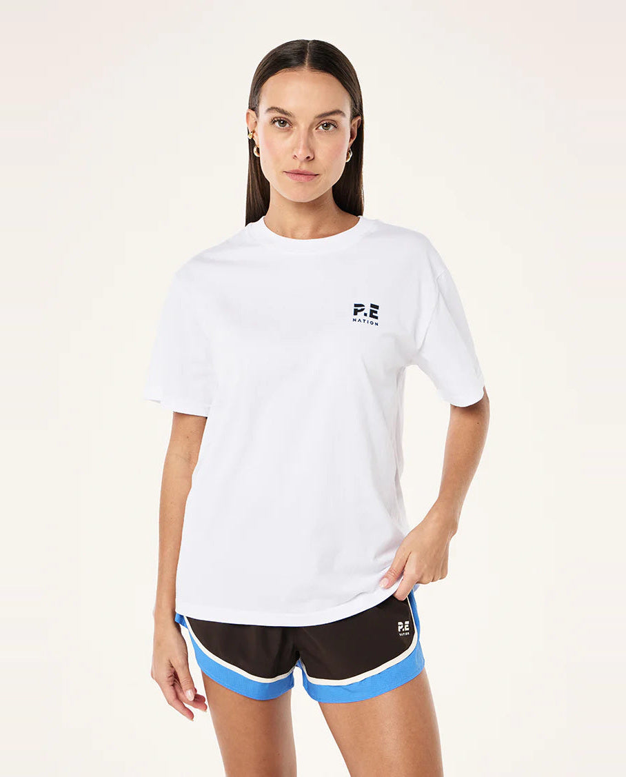 Woman wearing a white t-shirt with a logo and black shorts with blue accents on a white background