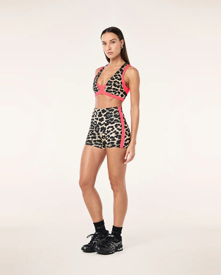 Woman wearing a leopard print sports bra and shorts with pink accents on a white background