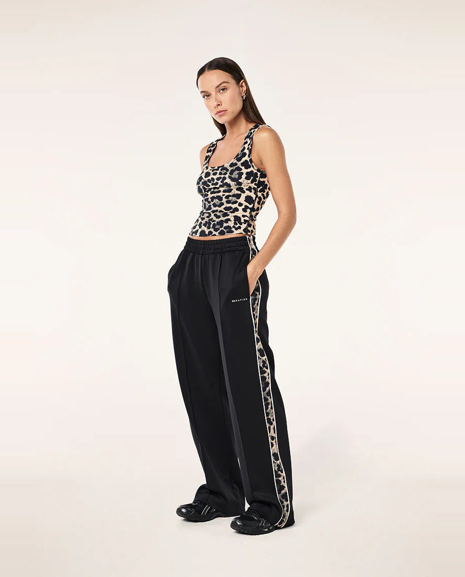 Woman wearing a leopard print top and black pants with a side stripe on a white background