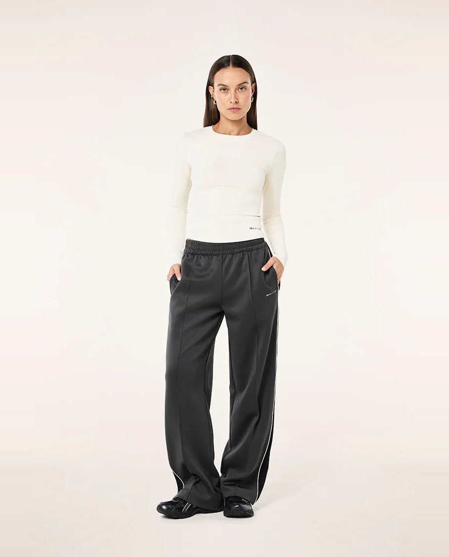 Person wearing a white sweater and black pants on a light pink background