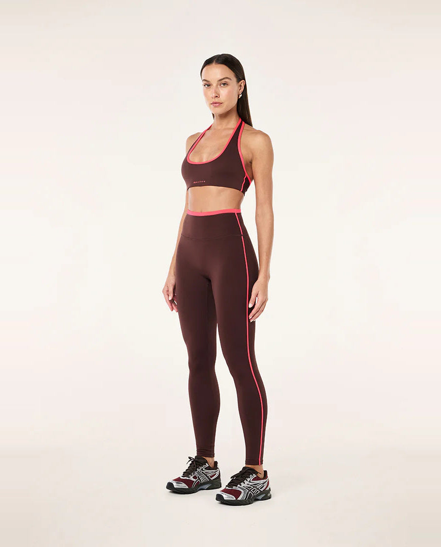 Woman wearing a brown sports bra and leggings with pink accents on a white background