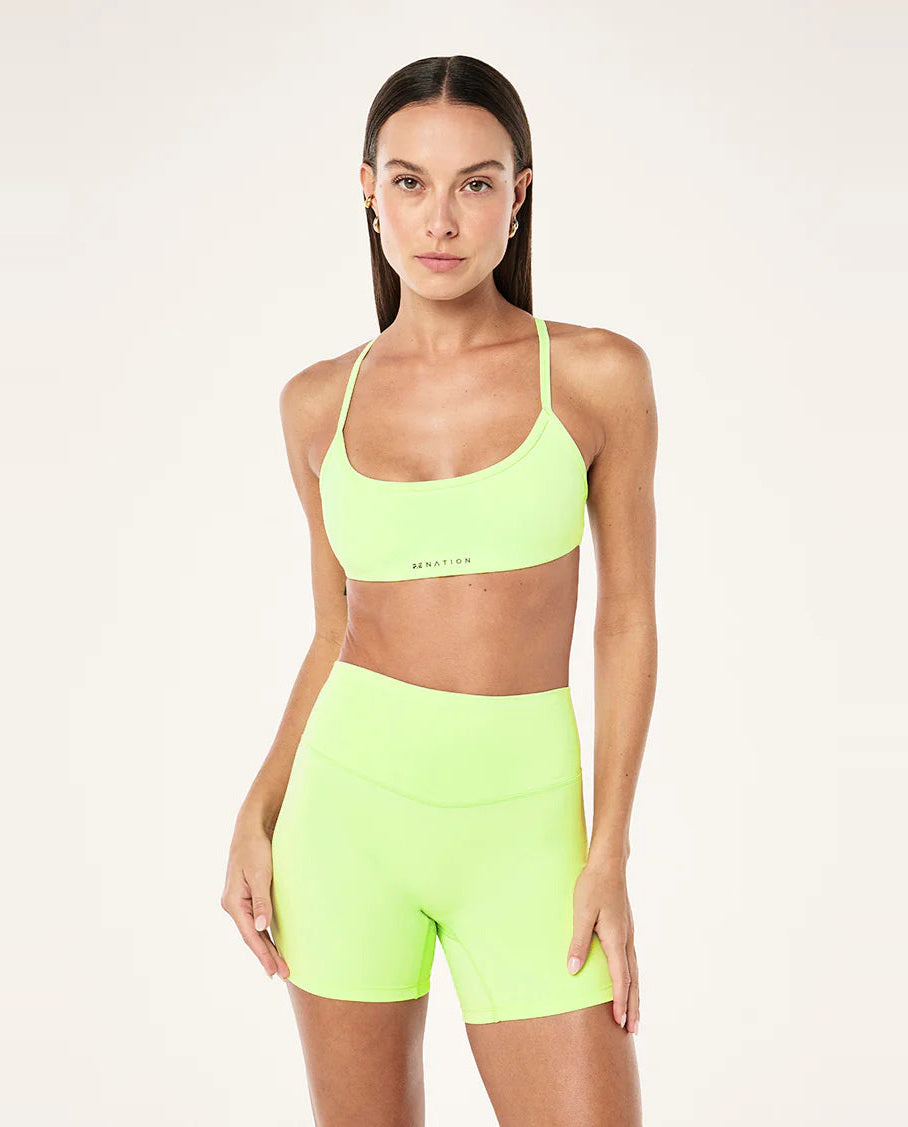 Woman wearing a neon green sports bra and shorts set on a light background