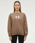 A woman wearing a beige crew neck sweatshirt with 'P.E NATION' branding on the front.