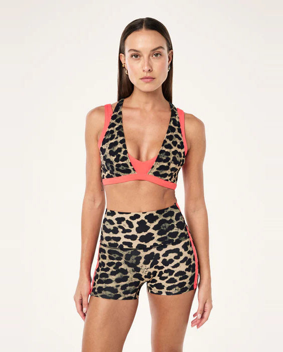 Woman wearing a leopard print sports bra and shorts with pink accents on a white background