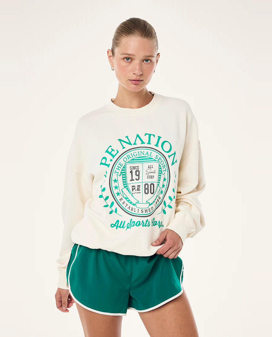 Person wearing a cream sweatshirt with green text and green shorts on a white background