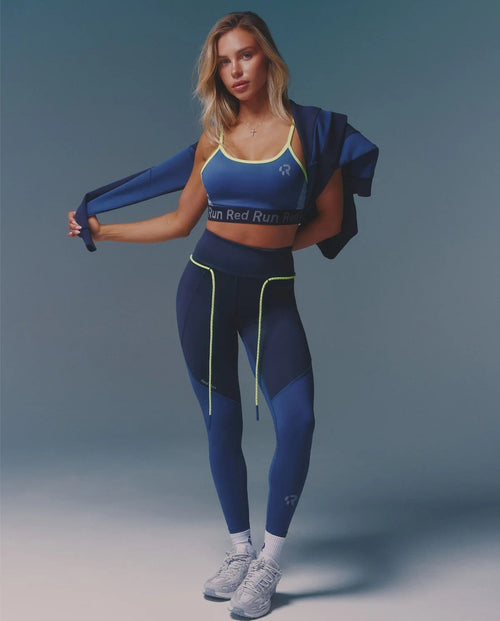 Woman in blue athletic outfit with a jacket on a gradient background