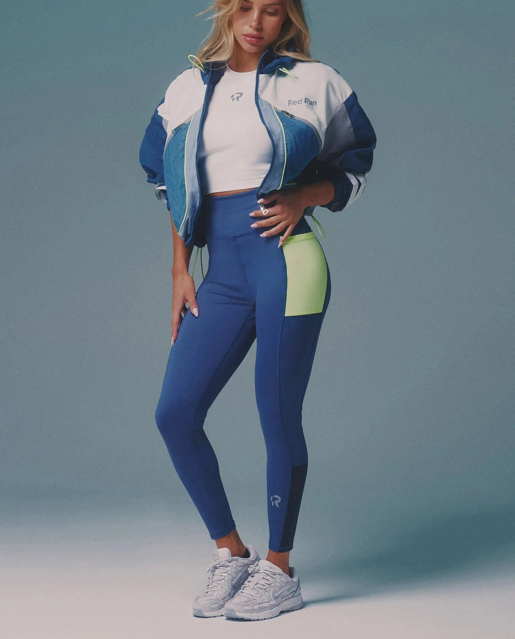 Woman wearing a blue and white athletic outfit with a green accent on a gray background