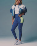 Woman wearing a blue and white athletic outfit with a green accent on a gray background