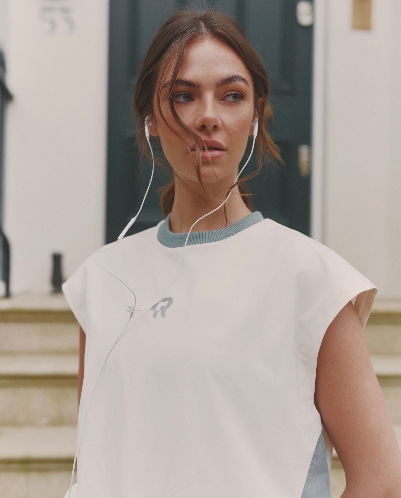 Woman wearing a light-colored sleeveless top with a brand logo, standing outdoors.