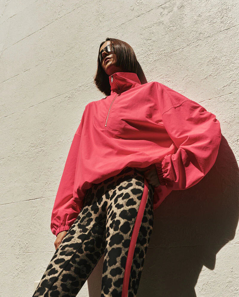 Person wearing a bright pink jacket and leopard print pants against a light gray wall.