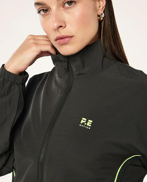 Woman wearing a grey  jacket with a logo on a light pink background