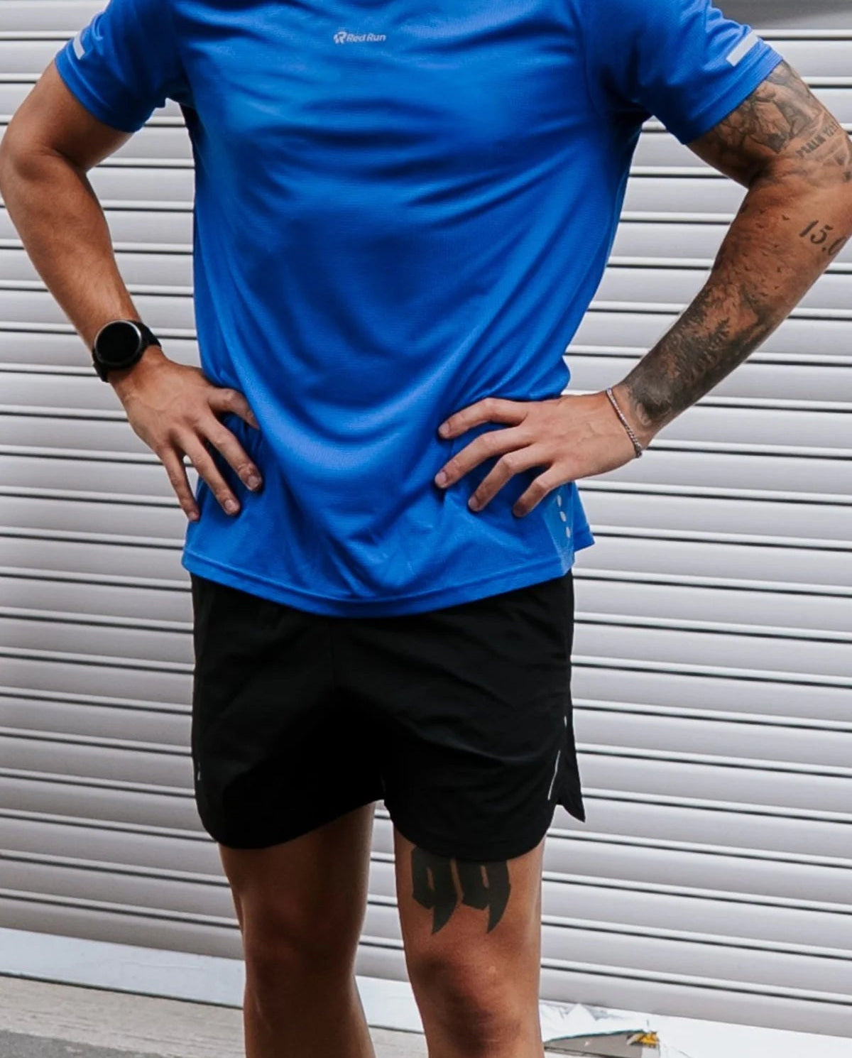Person wearing a blue athletic shirt and black shorts standing against a metallic background