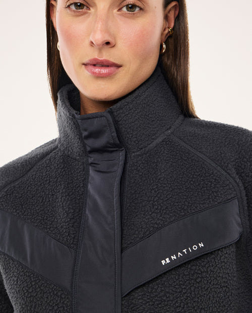 Woman wearing a dark blue fleece jacket with a visible brand logo on a light background