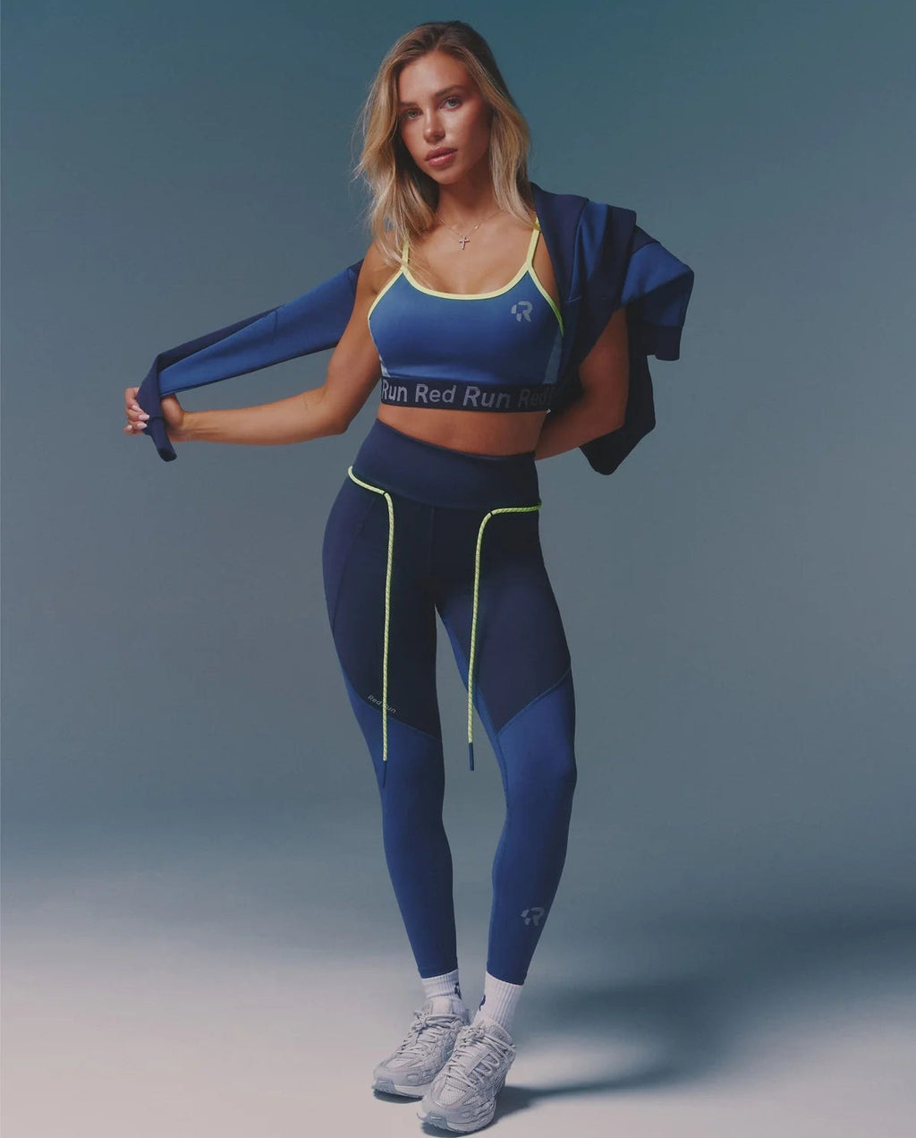 Woman in blue athletic outfit with a jacket on a gradient background