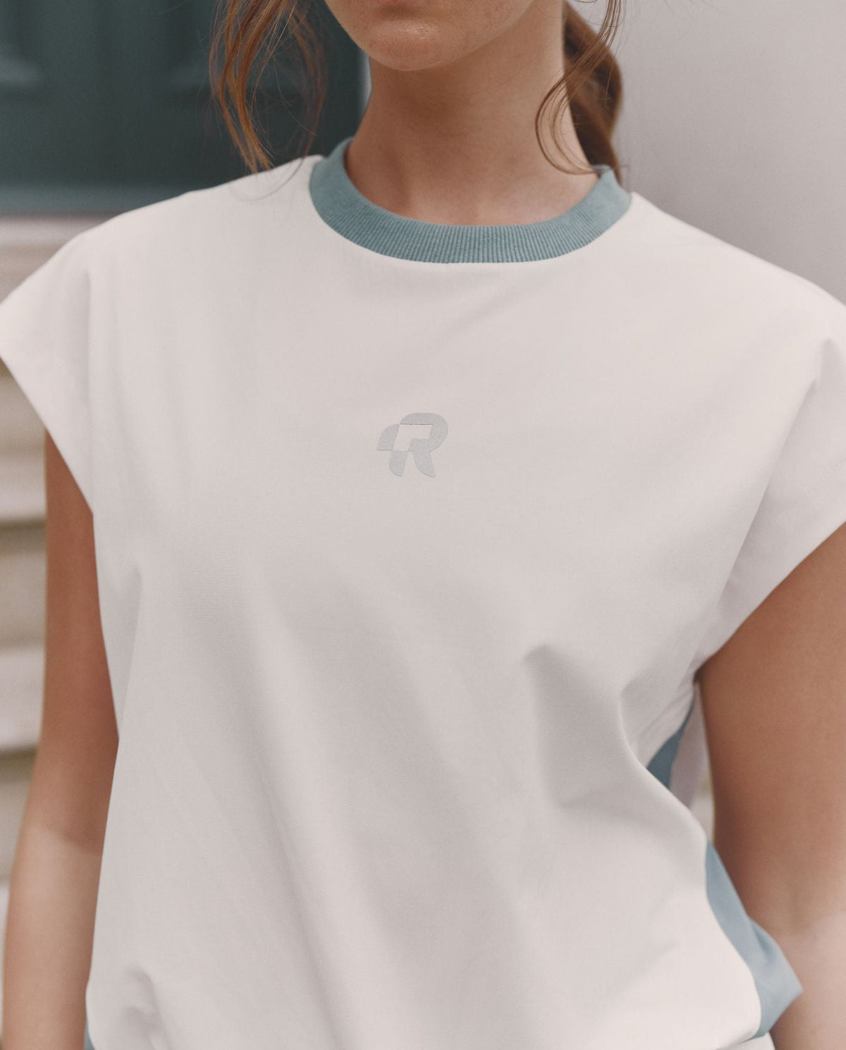 Person wearing a white top with blue trim and a logo on a blurred background