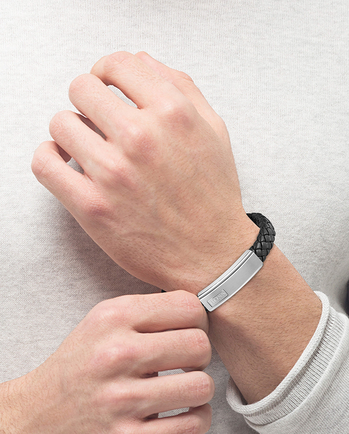 Man fastening a Boss Lander bracelet. The black braided leather strap has a stainless steel cap with the BOSS logo.