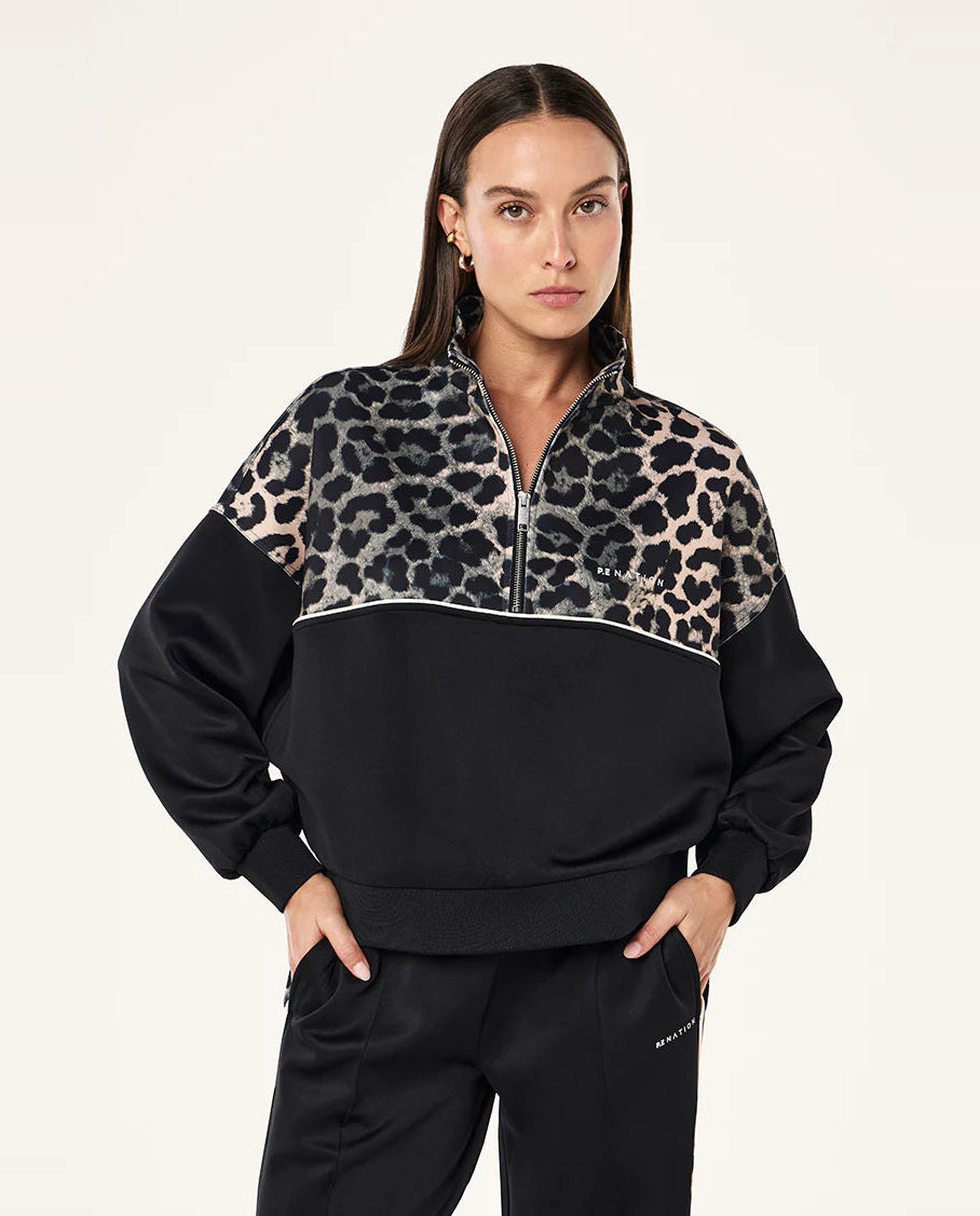 Woman wearing a black and leopard print half-zip sweatshirt on a white background