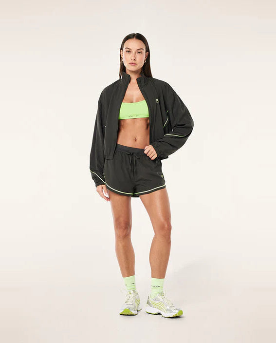 Woman wearing a grey jacket, green sports bra, and shorts on a white background