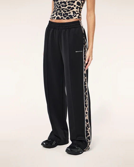 Person wearing black track pants with a leopard print side stripe on a white background