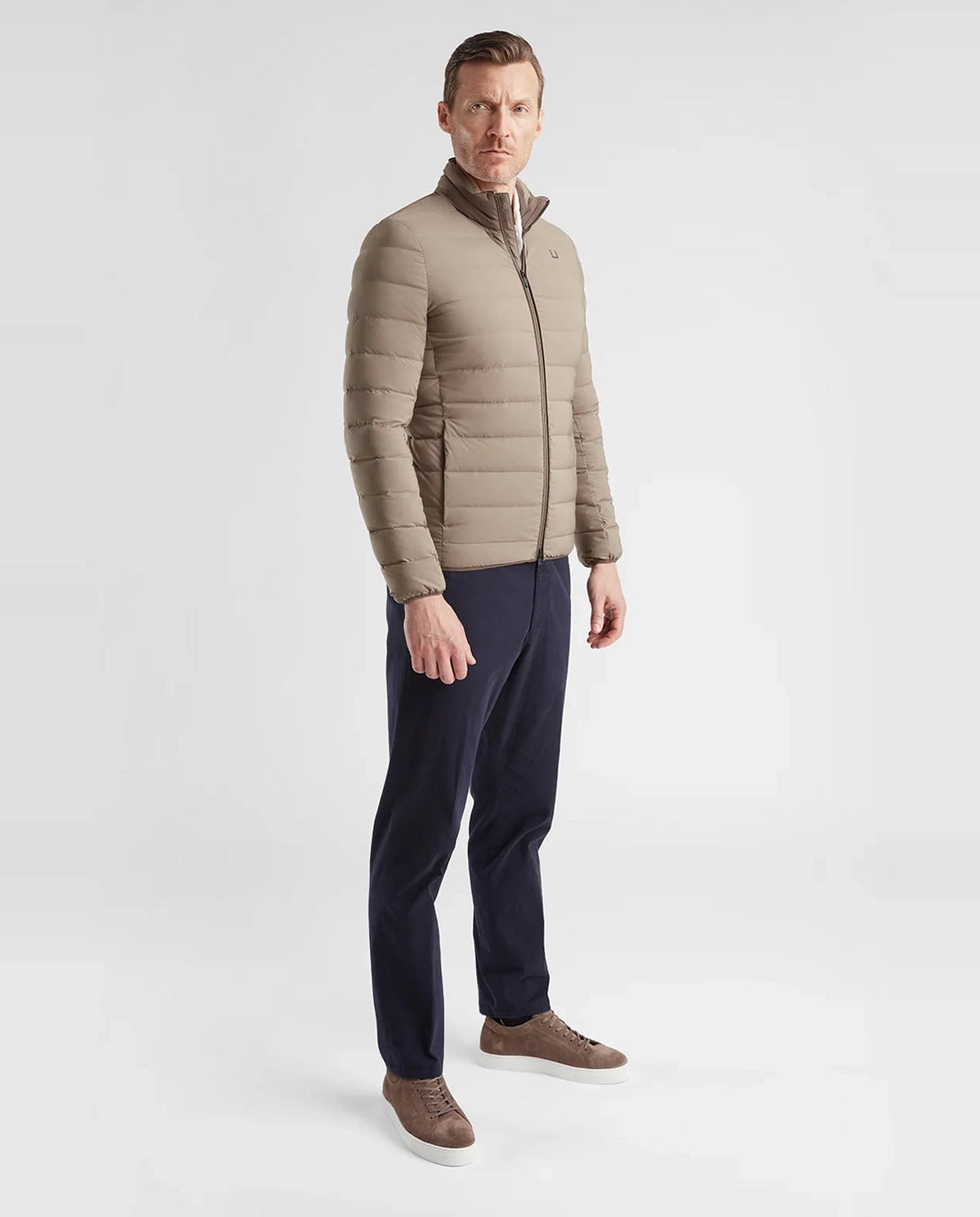 Man wearing a UBR beige quilted jacket, navy pants, and brown shoes on a white background