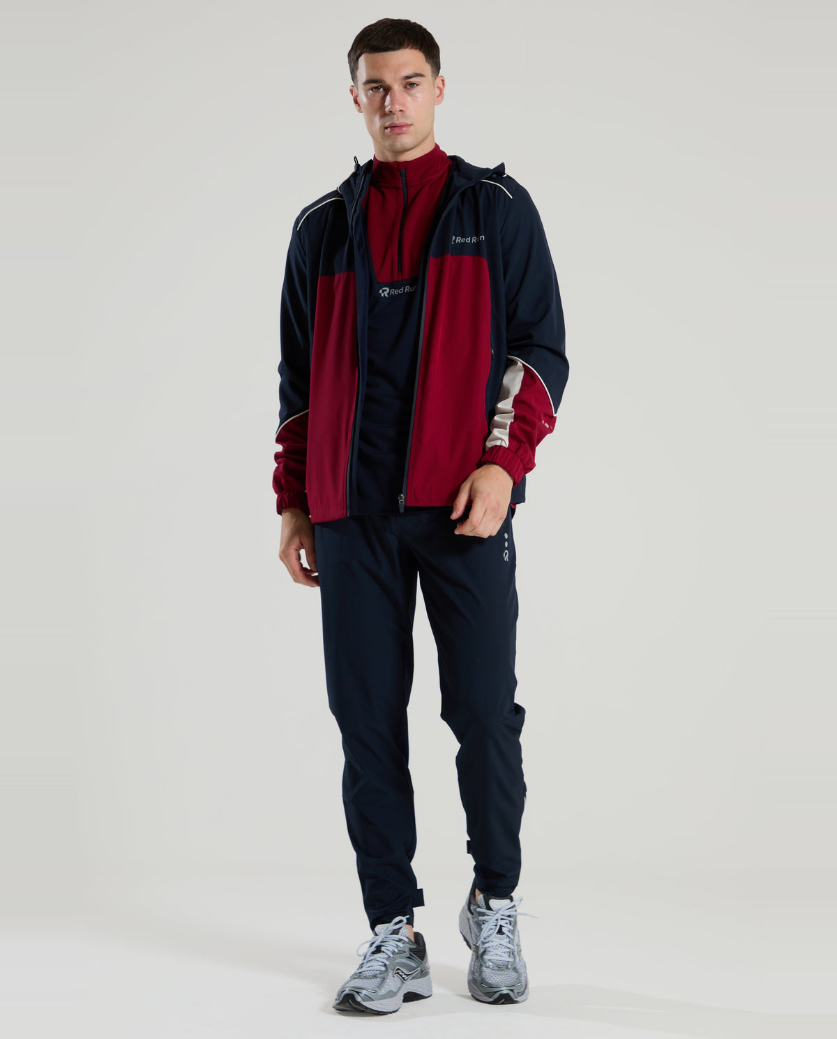Man wearing a red run burgundey and navy tracksuit with a logo on a white background