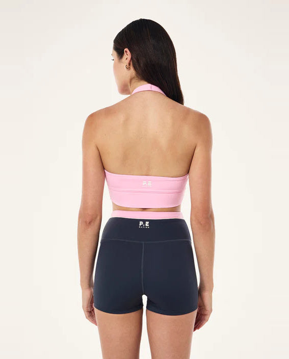 Woman wearing a pink sports bra and black shorts on a white background