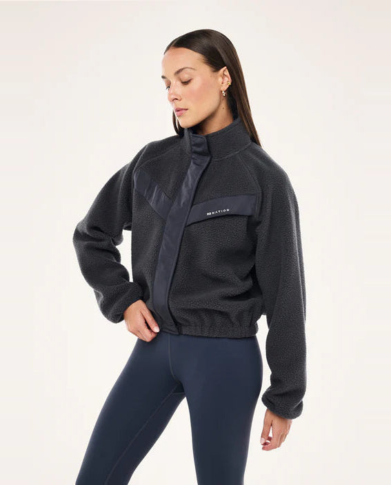 Woman wearing a dark blue fleece jacket with a brand logo on a white background
