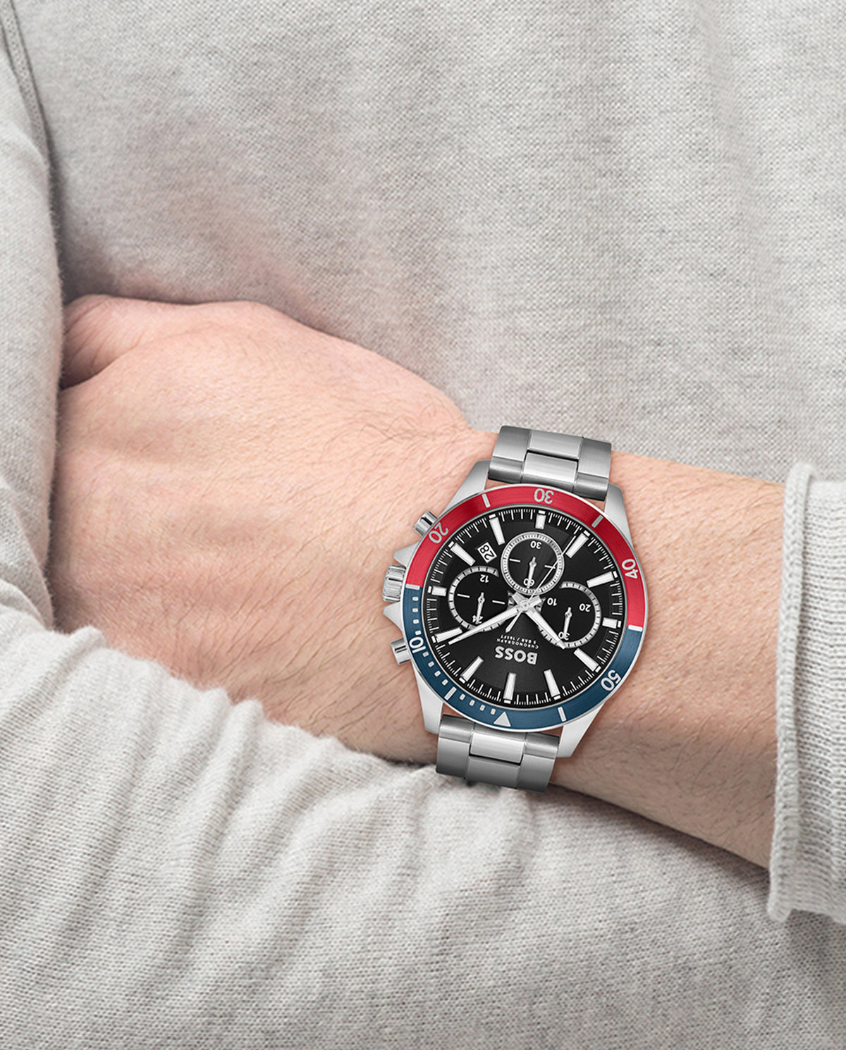 A stainless steel BOSS Troper chronograph watch on a wrist, displaying its black dial and red and blue bezel details.