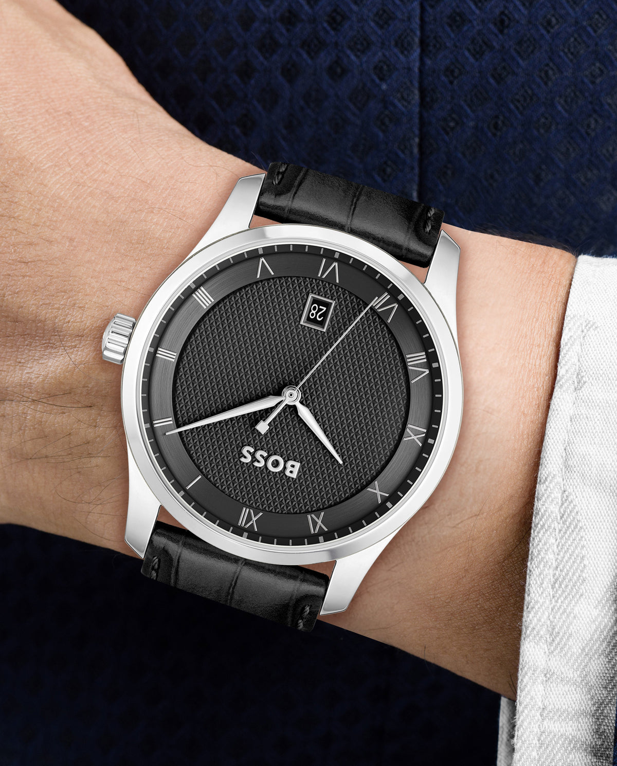 Close-up of a BOSS watch on a wrist, showcasing the black textured dial, stainless steel case, and black leather band.