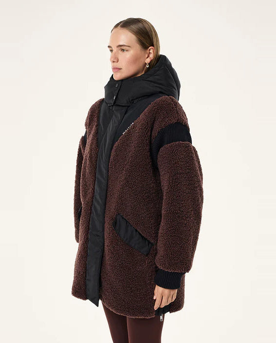 Woman wearing a brown teddy coat over a black jacket on a white background