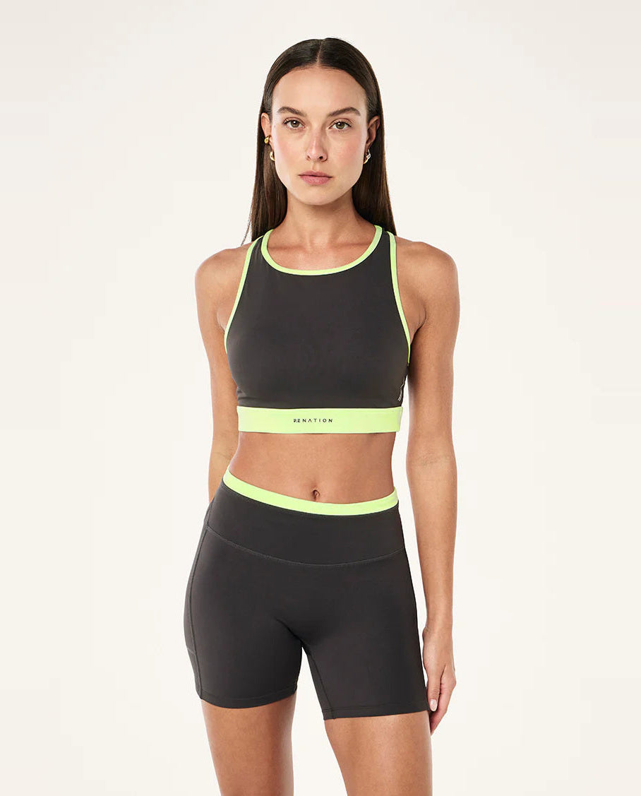 Woman wearing a grey sports bra and shorts with neon green accents on a white background