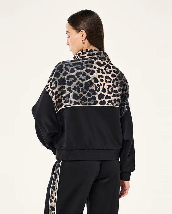 Person wearing a black tracksuit with leopard print details on a plain background