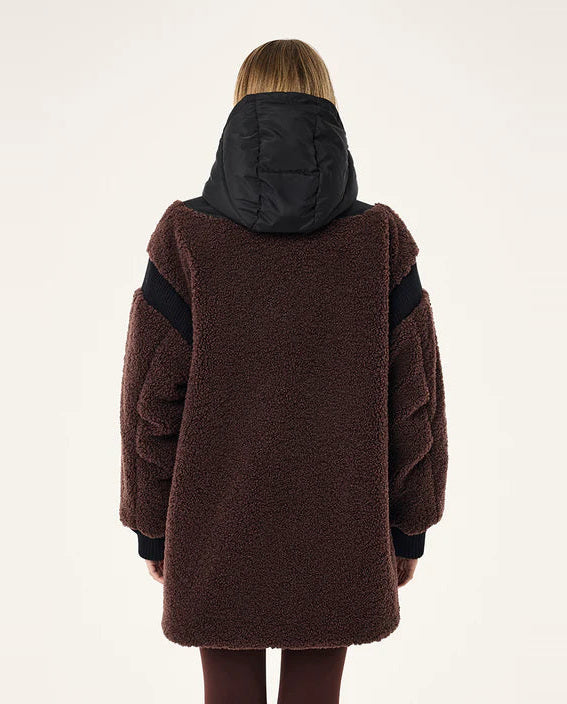 Person wearing a brown coat with black sleeves on a white background