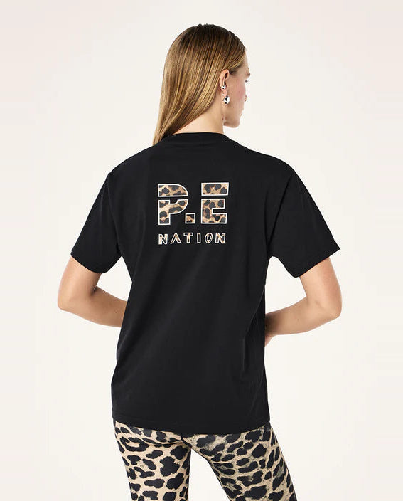 Person wearing a black t-shirt with 'P.E. Nation' text on the back, standing against a light pink background.