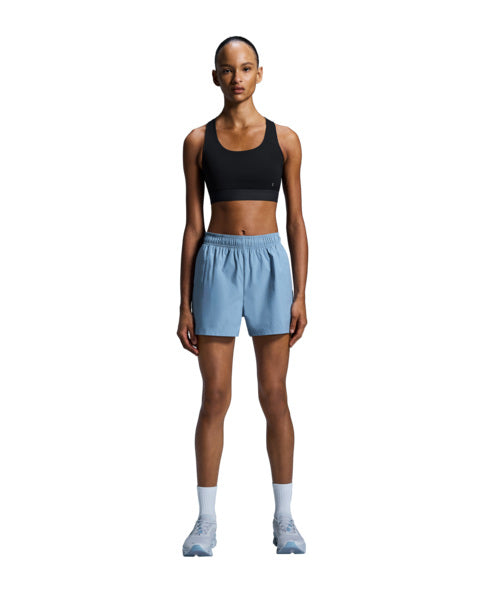 Woman wearing a black sports bra and light blue shorts on a white background