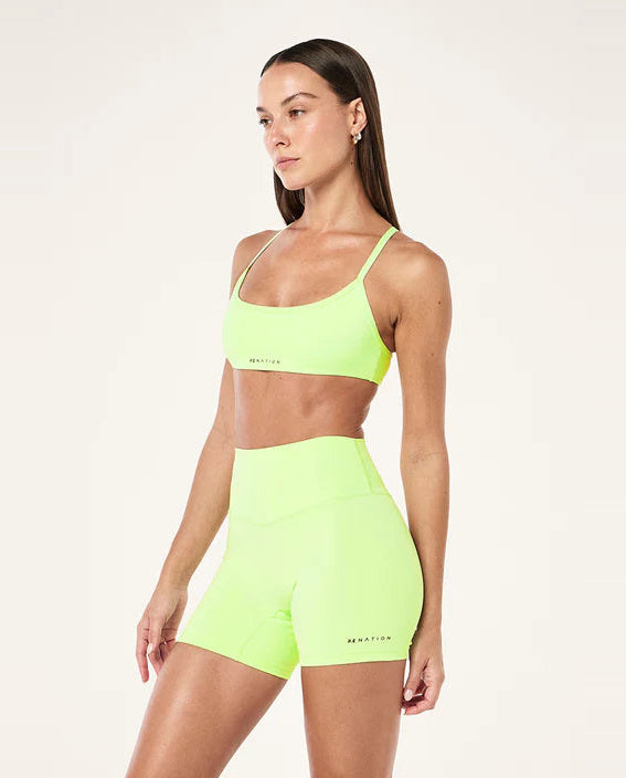 Woman wearing a neon green sports bra and shorts set on a white background