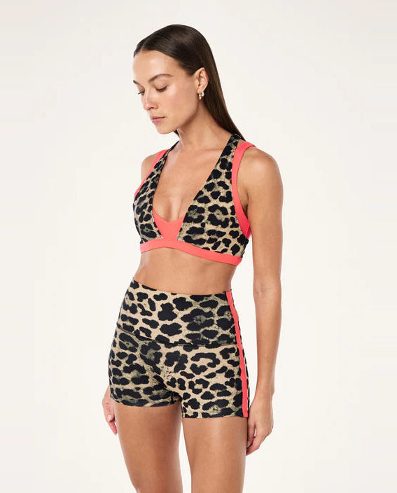 Woman wearing a leopard print sports bra and shorts with pink accents on a white background