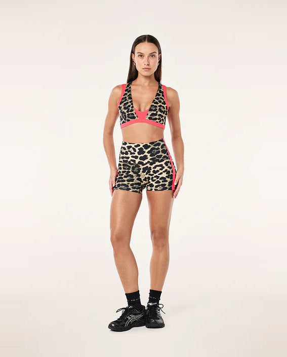 Woman wearing a leopard print sports bra and shorts set with pink accents on a white background