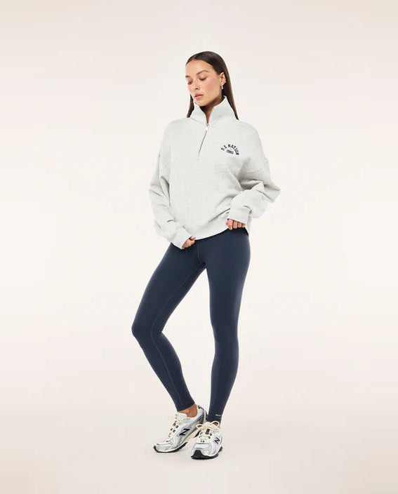 Woman wearing a white sweatshirt and dark blue leggings on a light pink background