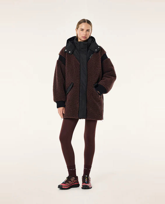 Person wearing a brown coat with black accents on a white background