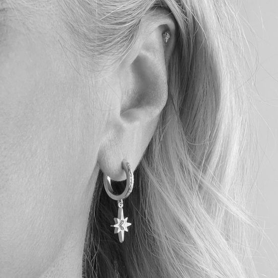 Close-up of an ear with two earrings: a hoop earring with a star charm and a small stud.