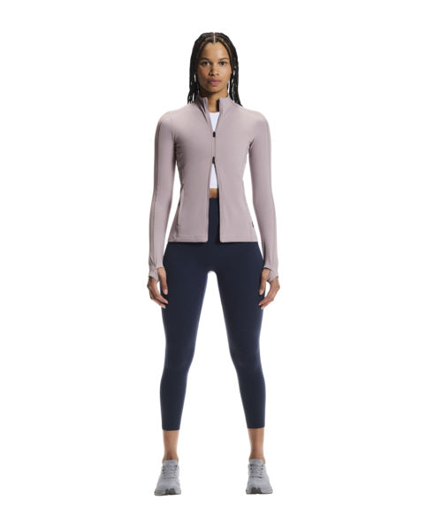 Woman wearing a light pink long-sleeve athletic jacket and dark blue leggings on a white background