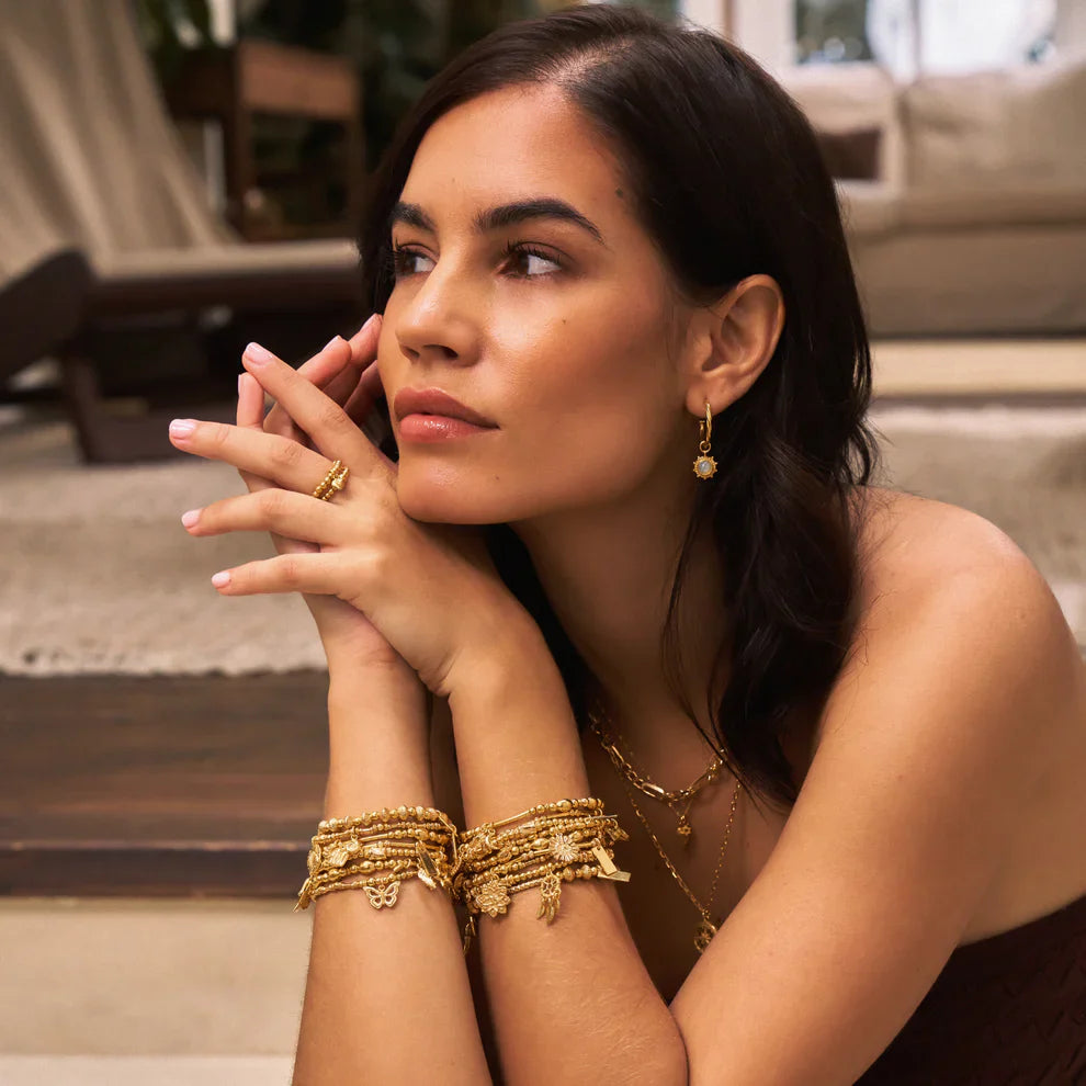 Woman wearing golden jewelry with multiple bracelets, earrings, ring, and necklace.